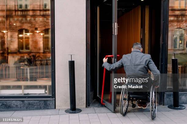 rear view of disabled mature man sitting on wheelchair while entering in store - entering shop stock pictures, royalty-free photos & images