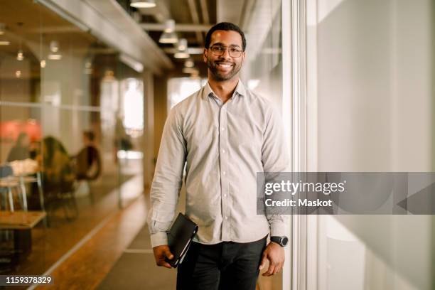 portrait of smiling sales executive standing in corridor at work place - man in black shirt stock pictures, royalty-free photos & images