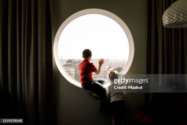 siblings by window in hotel room - round window curtains stock pictures, royalty-free photos & images