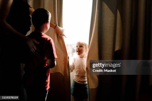 girl standing by window looking at mother with boy in hotel room - family holidays hotel stock pictures, royalty-free photos & images