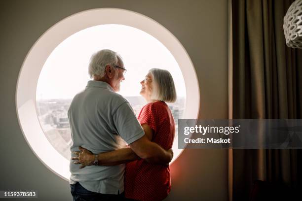 senior couple embracing while standing by window in hotel room - people circle stock-fotos und bilder