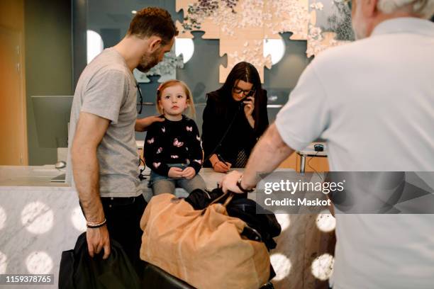 father talking to girl sitting on desk at reception in hotel - festnetztelefon stock-fotos und bilder