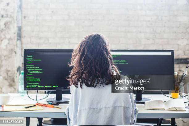 rear view of female computer hacker coding at desk in creative office - vista posteriore foto e immagini stock