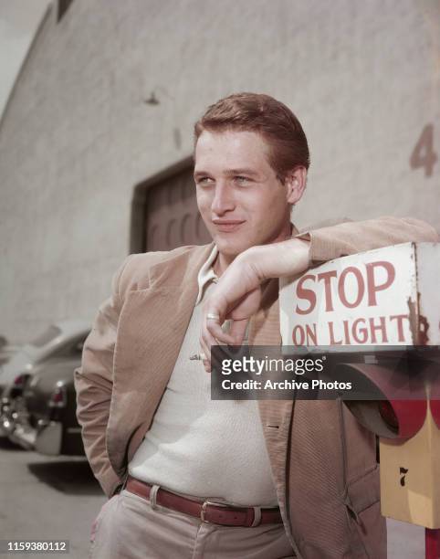 American actor Paul Newman leaning on a sign which reads 'Stop on Light' at a film studio during the filming of 'The Silver Chalice', circa 1954.