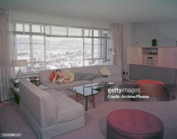 American actor Charlton Heston reading a book in a Los Angeles apartment, USA, circa 1950.
