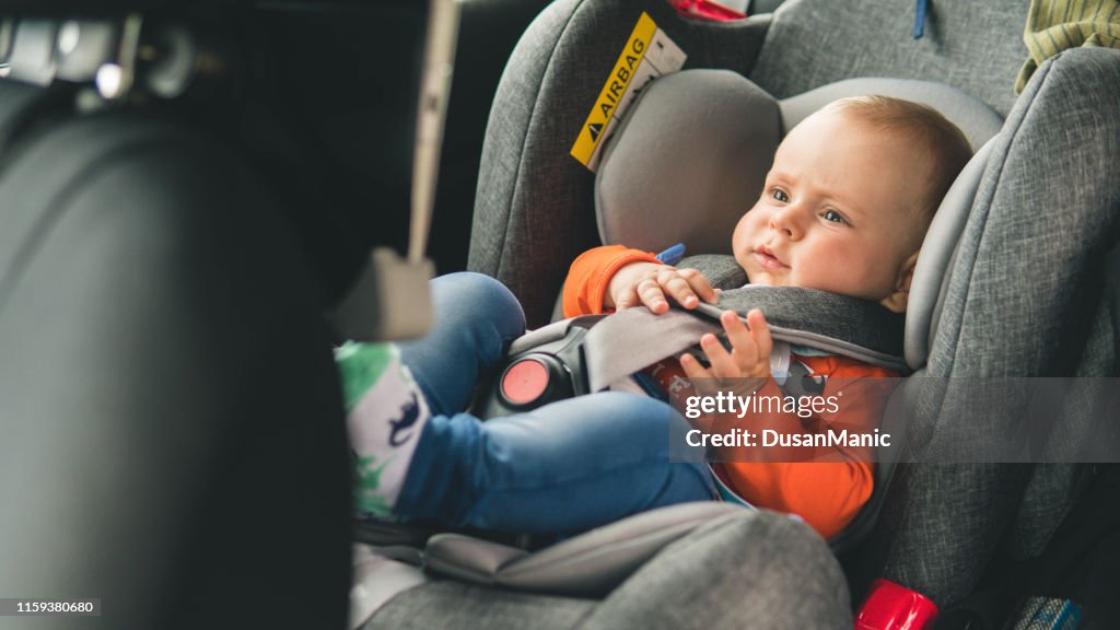 O bebê senta-se no assento de carro para a segurança.