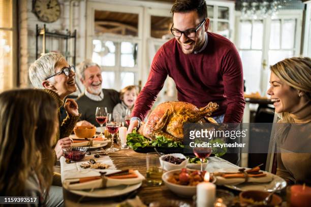 young happy man serving thanksgiving turkey for his family at dining table. - thanks giving stock pictures, royalty-free photos & images