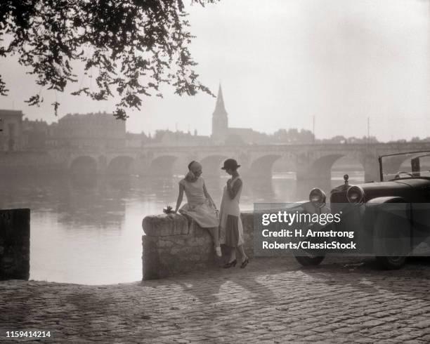 1920s TWO YOUNG WOMEN WITH ANTIQUE AUTOMOBILE SITTING STANDING TOGETHER TALKING BY STONE WALL LOIRE RIVER VALLEY FRANCE