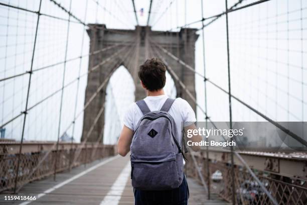 duizendjarige man met rugzak lopen over de brooklyn bridge - new york tourist stockfoto's en -beelden