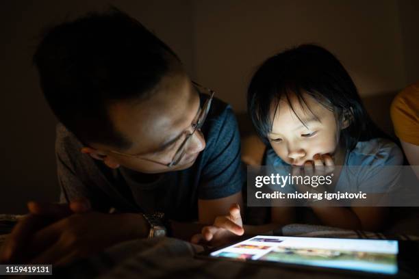 father and daughter using tablet before sleeping - beautiful chinese girl stock pictures, royalty-free photos & images