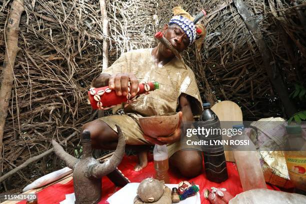 Chief Baykuh, a traditional healer in his shrine at Magbumoh village mixes herbs into potions on December 1, 2018. - In his mouth he holds an animal...