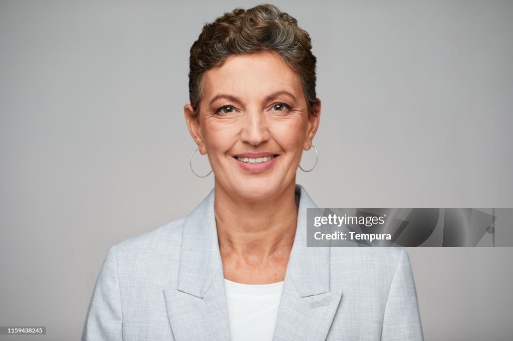 Middle aged sophisticated businesswoman studio headshot, wearing a suit.