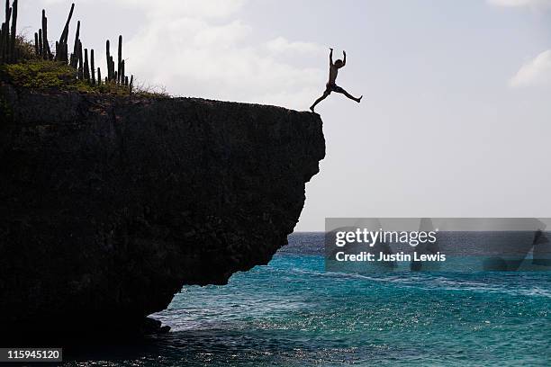man jumping off a cliff into the ocean. - salto desde acantilado fotografías e imágenes de stock