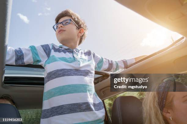 happy boy enjoying freedom on sunroof of car - sunroof stock pictures, royalty-free photos & images