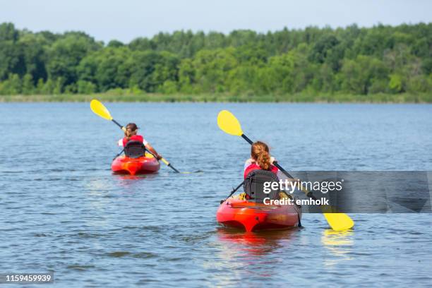 two young girls kayaking on lake in summer - family red canoe stock pictures, royalty-free photos & images