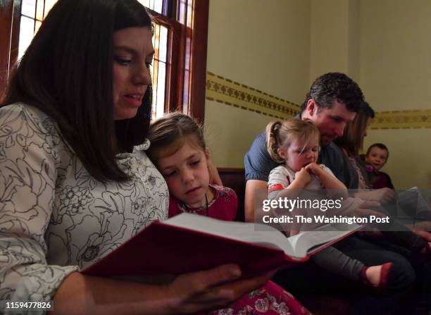 Sarah Krocak, holding her daughter Ella and her husband Marty, holding their other daughter Delaney try to sing along from the hymnal during a Palm...