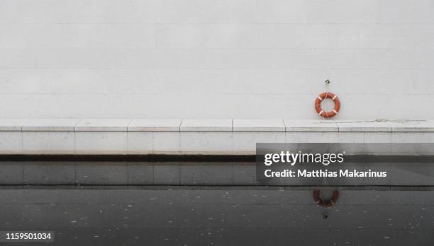 life belt in a urban city scene on a modern concrete wall and with river reflection - red wall stockfoto's en -beelden