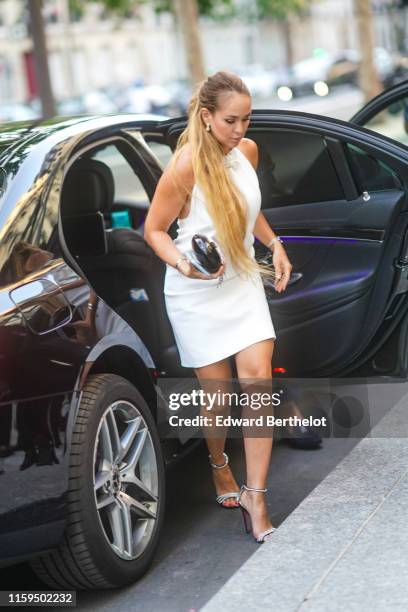 Guest wears earrings, a white halter mini dress, a black clutch, rhinestone embellished strappy heeled sandals, , outside AMFAR dinner, during Paris...