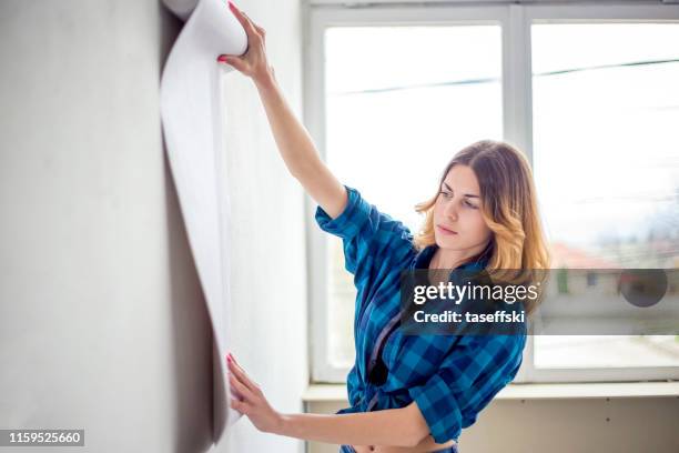 jonge vrouw kiezen huis behang - vrouw behangen stockfoto's en -beelden