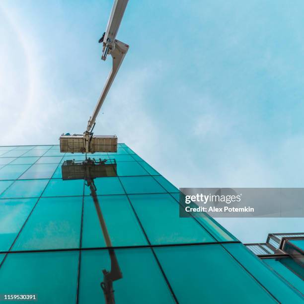 high-altitude work. team of blue-collar workers working on the office building glass facade using the lifting platform. - facade cleaning stock pictures, royalty-free photos & images