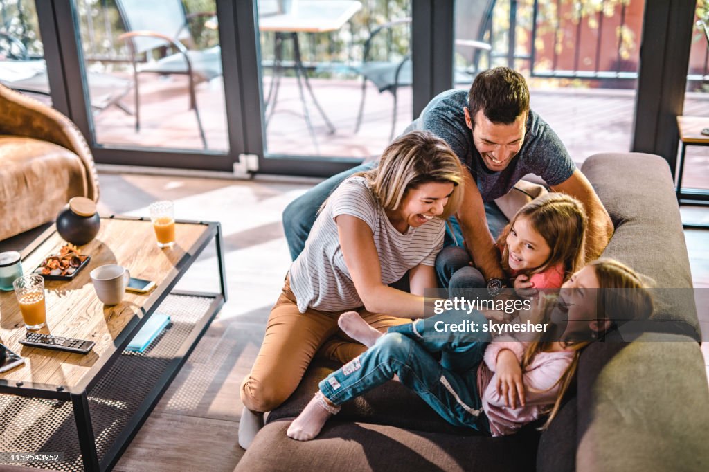 Above view of playful parents tickling their daughters at home.