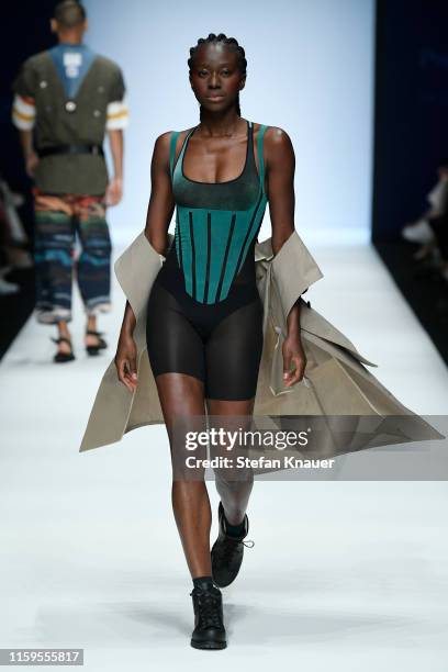 Model wearing a coat by Velvet Novel, sports bra & body & socks by Wolford, underwear by Kora Mikino and shoes by Haferl walks the runway at the...