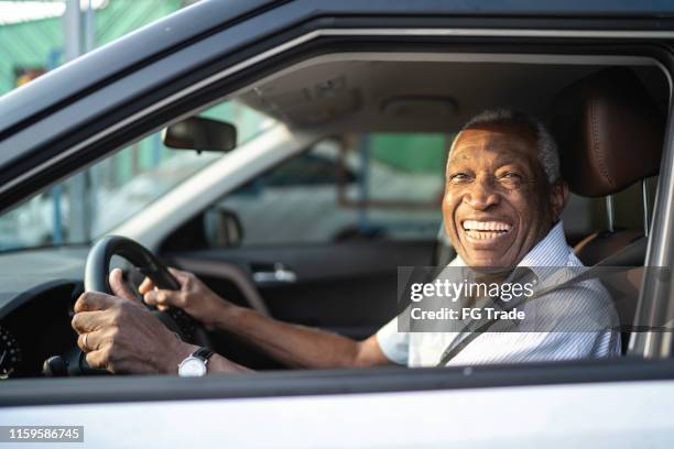 lächelnder senior afro mann fährt ein auto und schaut in die kamera - altes auto stock-fotos und bilder