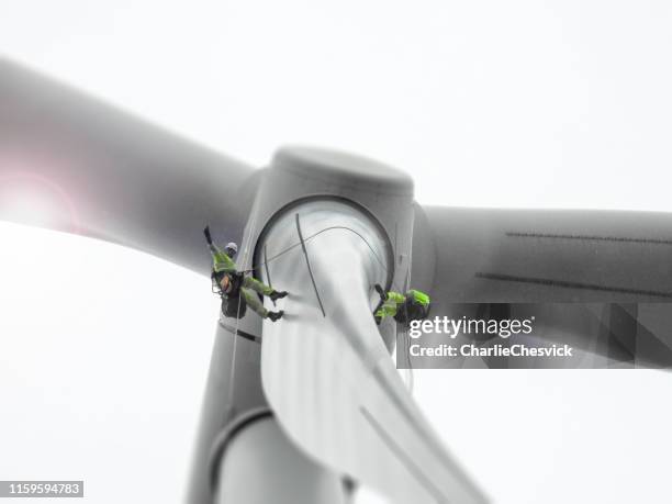 zwei seilzugangstechniker bei der inspektion und dem winken von windturbinenschaufeln - windmill stock-fotos und bilder