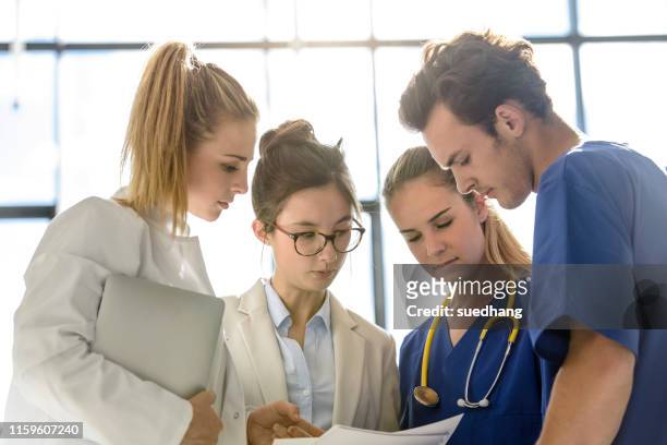 young female and male junior doctors looking at medical records in hospital - ジュニアドクター ストックフォトと画像