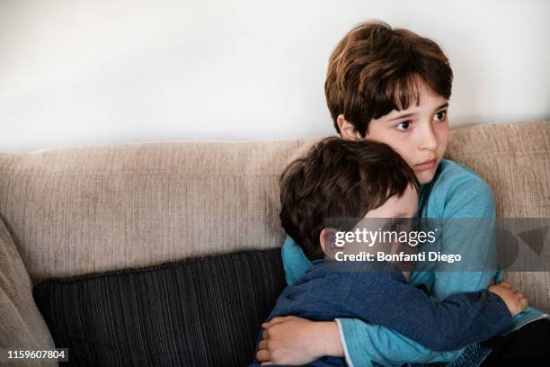 big brother hugging toddler, staring in disbelief on sofa - big bang stockfoto's en -beelden