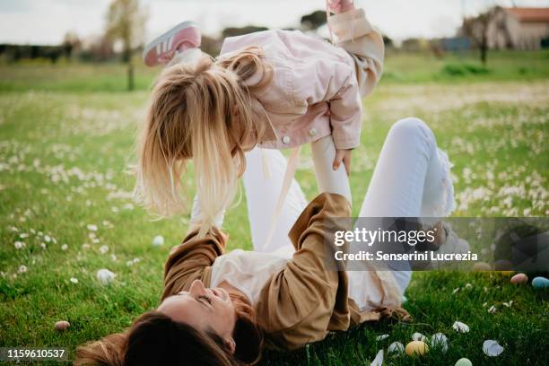 mother lying on back holding up daughter in wildflower field after easter egg hunt, arezzo, tuscany, italy - familys the lying game season two ストックフォトと画像