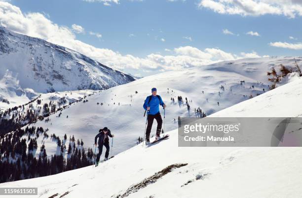 mature skiing couple moving up snow covered mountain,  styria, tyrol, austria - tirol deelstaat stockfoto's en -beelden