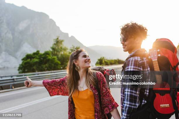 young couple asking for passage by car, hitch-hiking. - hitchhiking 個照片及圖片檔