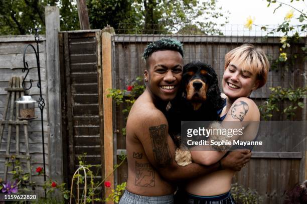 A young LGBT couple in the garden hugging a dog and laughing