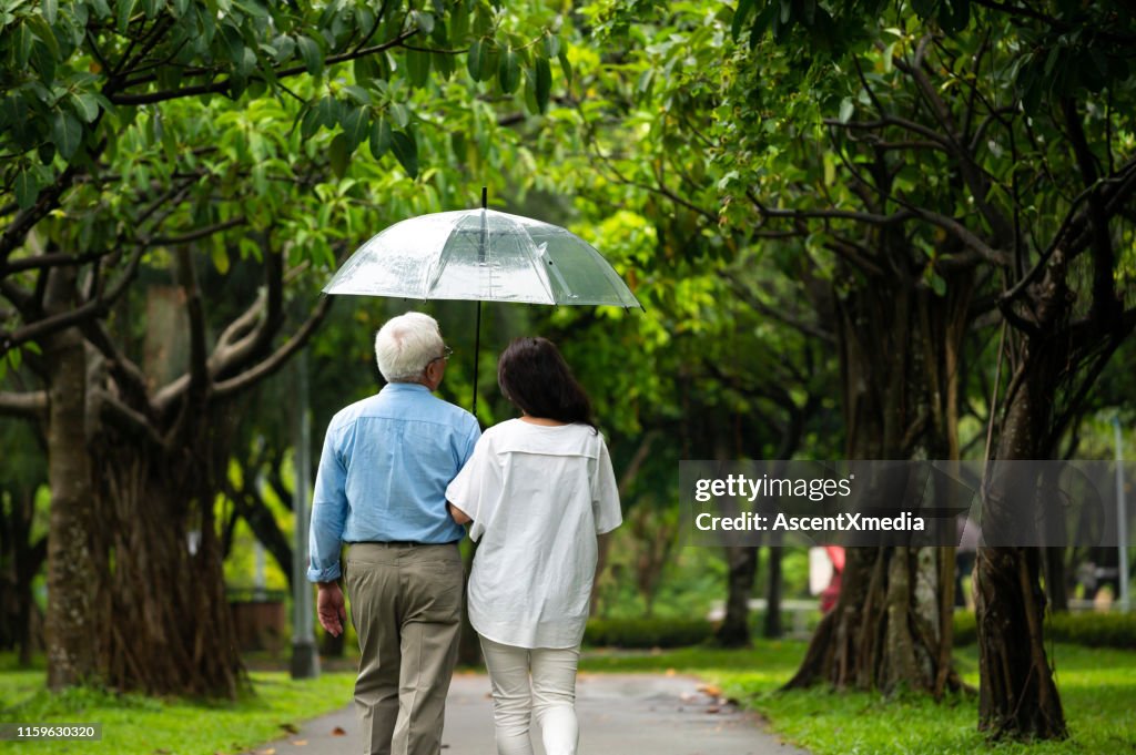 Senior couple walking in park during rainy season
