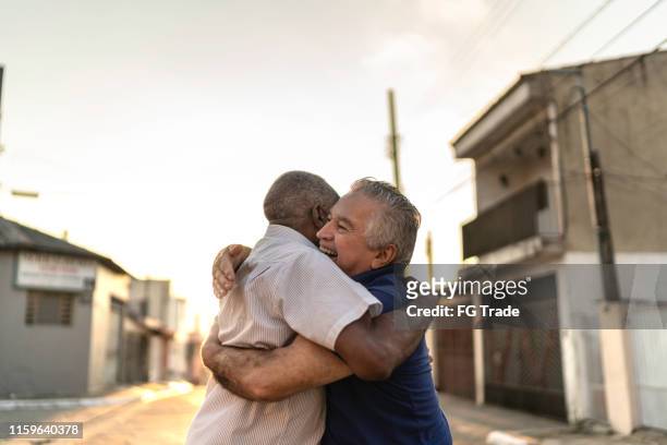 senior friends greeting each other on the street - man embracing stock pictures, royalty-free photos & images