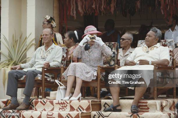 Queen Elizabeth ll taking a photograph with her gold Rollei camera sitting alongside Prince Philip during their tour of the South Pacific, in Tuvalu,...