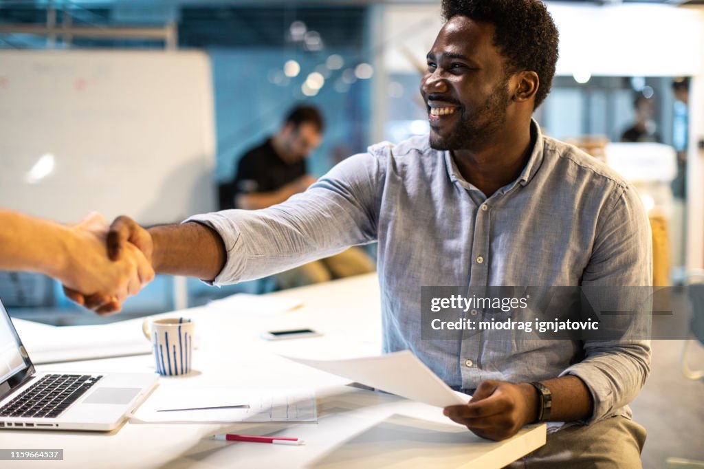 Homme noir se serrant la main avec la personne méconnaissable au travail