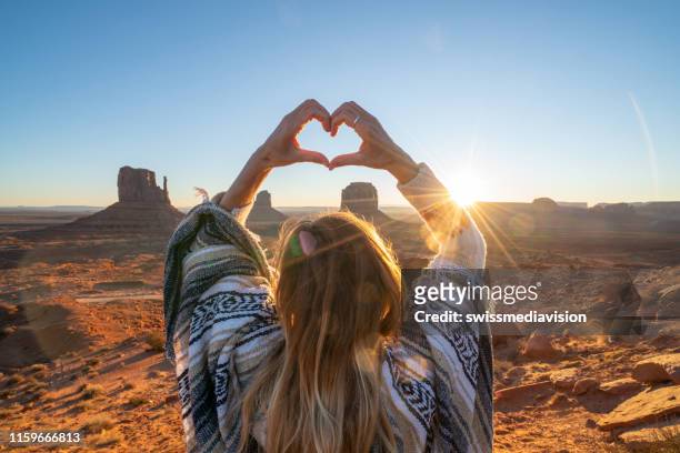 junge frau in der amerikanischen wüste machen herz form rahmen mit händen liebevolle roadtrip abenteuer - monument valley stock-fotos und bilder