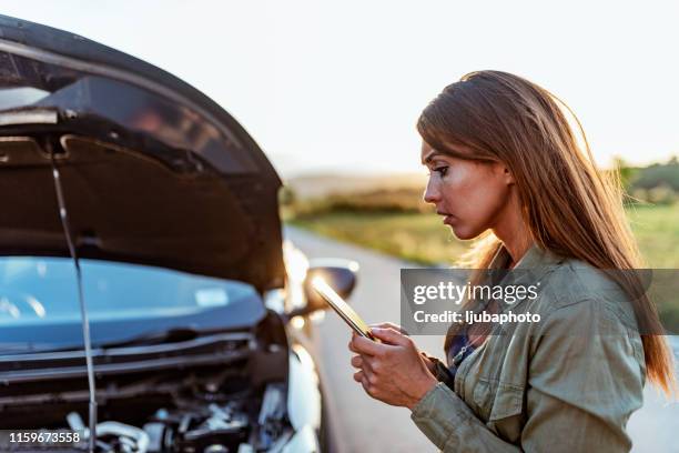 young woman typing text message on mobile phone next to her broken car - damaged phone stock pictures, royalty-free photos & images