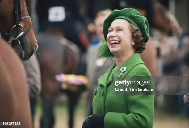 Queen Elizabeth II, wearing a green coat and matching hat, laughing as she attends the Royal Windsor Horse Show, held at Home Park in Windsor,...