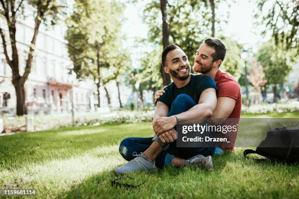 coppia gay - uomini millenari latino ed europei - che si godono nel parco in estate - uomo gay foto e immagini stock