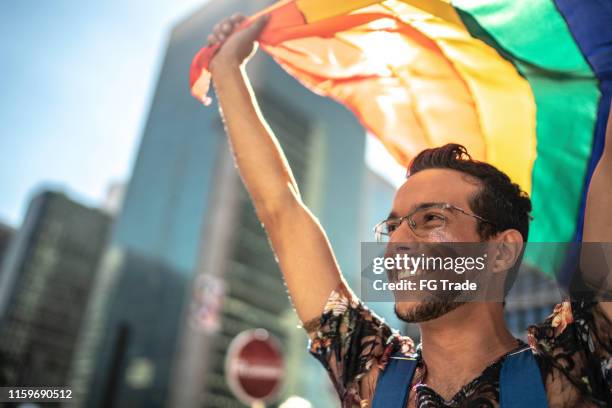 homem gay novo que prende a bandeira do arco-íris durante a parada do orgulho - desfiles e procissões - fotografias e filmes do acervo