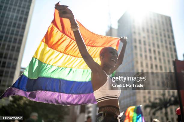 mujer lesbiana segura sosteniendo la bandera arco iris durante el desfile del orgullo - lgbtqia pride event fotografías e imágenes de stock