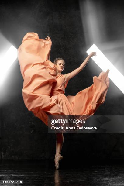 ballerina. a young dancer dressed in a long peach dress, pointe shoes with ribbons. performs a graceful, graceful dance movement on the background of the bright light of the window.  ballet studio. 3d - ballet dancers russia stockfoto's en -beelden