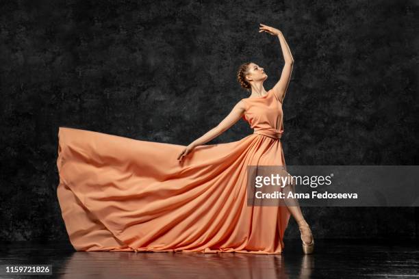 ballerina. a young dancer dressed in a long peach dress, pointe shoes with ribbons. performs a graceful, graceful dance movement. beautiful classic ballet. advertising ballet studio. volumetric photos - long dress stock-fotos und bilder