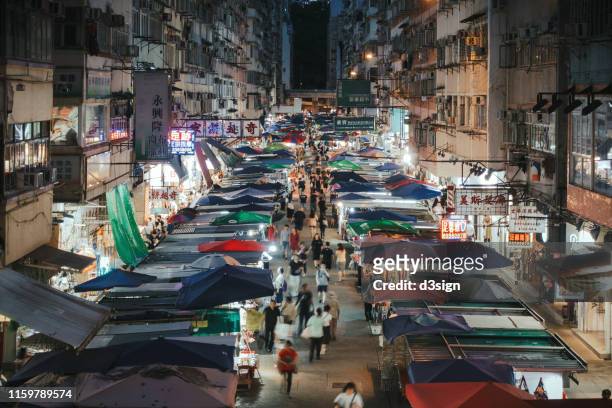 busy city street with local market stalls at night. tourists and locals shopping and exploring in mongkok, hong kong - hong kong community 個照片及圖片檔