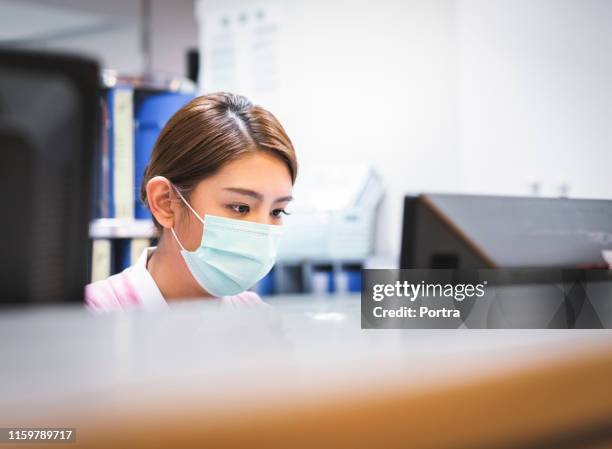 serious nurse using computer in hospital - asian receptionist stock pictures, royalty-free photos & images