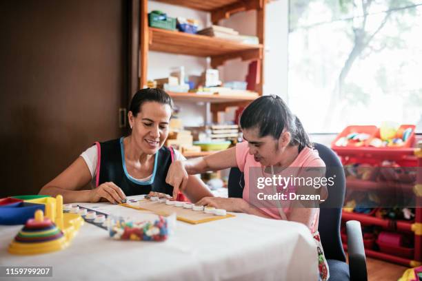 latina teacher playing with down syndrome woman - learning disability nurse stock pictures, royalty-free photos & images