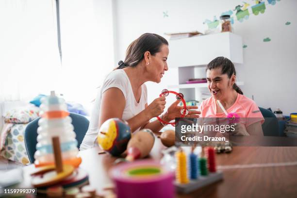 mature down syndrome woman in day care nursery, playing with teacher - learning disability nurse stock pictures, royalty-free photos & images